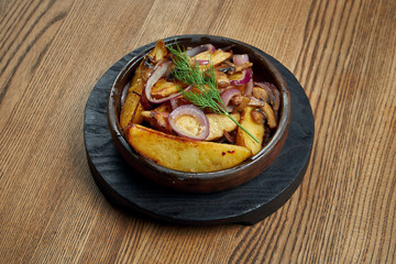 Oven-baked potato wedges with red onion and mushrooms. A classic side dish of Slavic cuisine. Vegetarian dish. Close up, wooden background