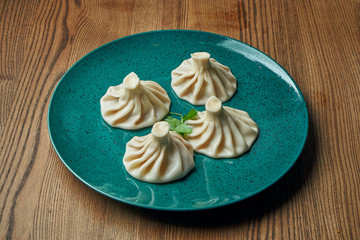 Appetizing homemade khinkali with different fillings (minced meat, cheese, vegetables or spinach) in a blue plate on a wooden background. Traditional Georgian cuisine. Georgian dumplings