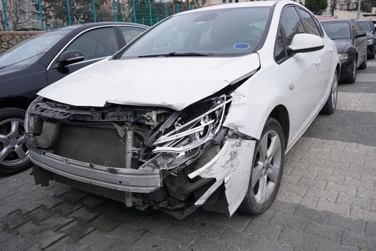 A parked crashed white car at street with broken headlights