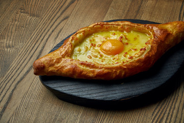 Close up view on tasty traditional Adjarian Khachapuri - open baked pie with melted salt cheese (suluguni) and egg yolk on wooden tray. Traditional georgian food