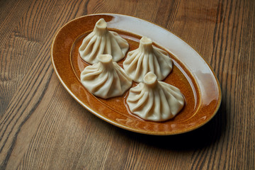 Appetizing homemade khinkali with different fillings (minced meat, cheese, vegetables or spinach) in a brown plate on a wooden background. Traditional Georgian cuisine. Georgian dumplings
