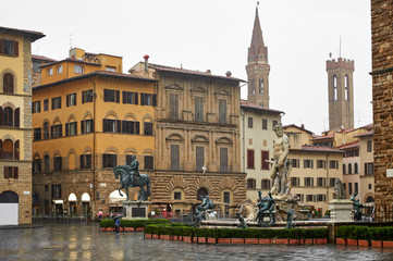 Fototapeta na wymiar Florence Italy. Piazza della Signoria with view at Neptune Fountain with bronze statues in rainy weather day and antique houses and tower.