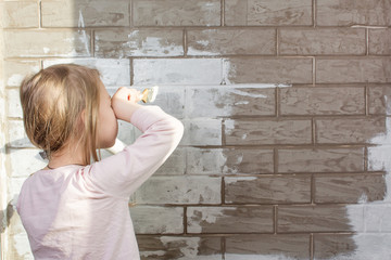 A little girl will paint a brick wall white. Wall painting, repairs in the house. The painter, the...