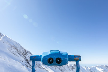 Touristic binoculars, device for sightseeing, stationary viewing binoculars, viewing binoculars with  coin operator, with view on beautiful snowy mountains on background, shoot taken with back light 