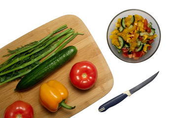 Fresh vegetarian salad cooking. Tomatoes, cucumber, paprika and greens in wooden cutting board