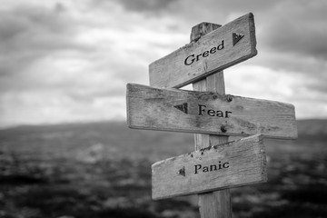 Greed, fear and panic text on wooden road sign outdoors. Black and white theme. To illustrate the...