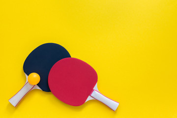 Red and black tennis ping pong rackets and orange ball isolated on a yellow background, sport...