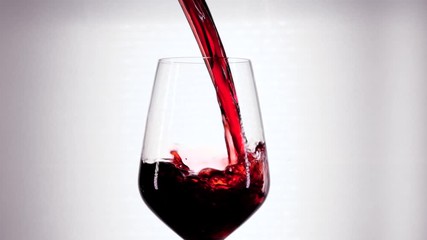 Slow motion of pouring red wine from bottle into goblet. Close-up of red wine forms beautiful wave in glass. Wine pouring in glass at white background. - Powered by Adobe