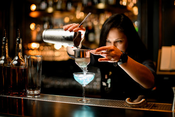 bartender pours cocktail from shaker into glass using sieve.