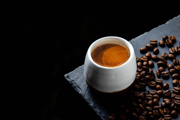 Fresh hot brewed espresso in white cup on black plate with roasted coffee beans