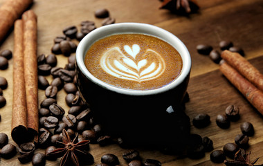 Cup of latte art barista coffee with cinnamon. Coffe with roasted beans on wooden background 