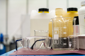 Clear plastic protection goggles next to empty glass and plastic containers in a science lab