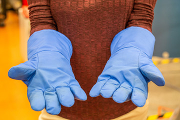 Female science student posing blue thick protection gloves in a science lab no face unrecognizable