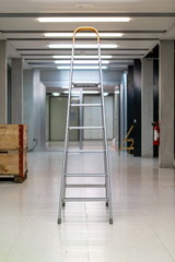 V shaped open ladder standing on a laboratory hallway corridor illuminated by neon lights shallow depth of field front view
