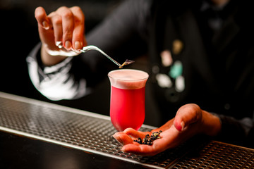 Bartender neatly hold tweezer with flower over cocktail glass.