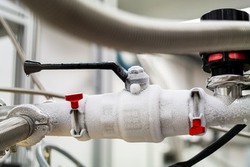 Obraz premium Frozen liquid nitrogen carrying pipes with a valve and black plastic lever close up in a science laboratory