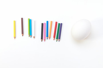 a snow white hen egg ready to be colored for Easter on a white background laying with colorful pencils