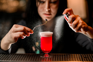 Bartender professionally hold tweezer with decoration over glass and spraying on it.