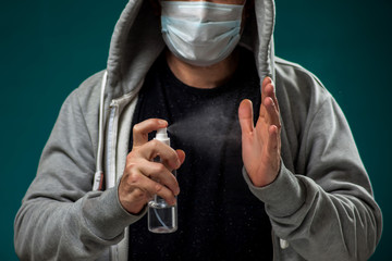A portrait of man with medical face mask using disinfectant spray on hands. People, medicine, healthcare concept. Coronavirus protection