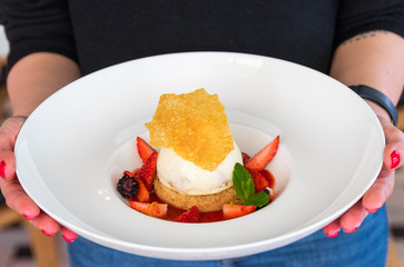 cheescake with ice cream and strawberries in a woman hands