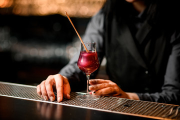 Nice pink cocktail in glass decorated with two sticks standing on bar.