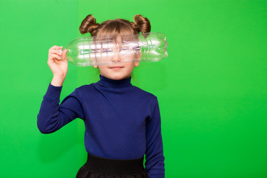 Little environmentalist girl isolated on green background looking through plastic bottle and shows interest in reducing plastic consumption and introducing an alternative