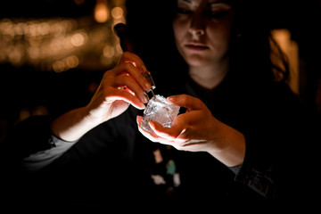 woman bartender with special device breaks pieces of ice.