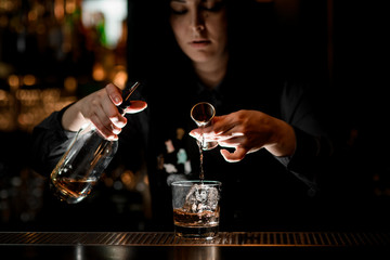 Girl bartender preparing alcoholic cocktail with ice.