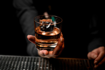 close-up of glass with alcoholic drink in bartender's hand.