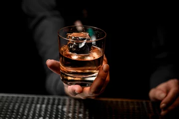 Foto op Plexiglas close-up of glass with alcoholic drink in bartender's hand. © fesenko