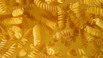 Freeze motion of flying uncooked italian pasta fusilli on golden background.