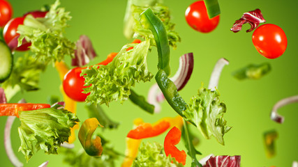 Flying vegetable salad isolated on green background. Healthy eating and lifestyle.
