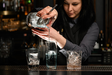 Professional woman bartender pours alcoholic cocktail into glass.