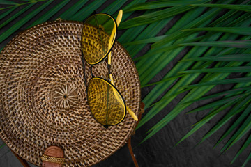 vacation flat lay background with strow hat, yellow glasses and palm leaves on black stone background