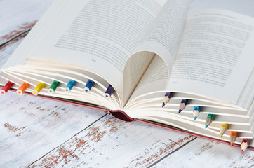 Rainbow of colored pencils that were inserted between the pages of an open textbook