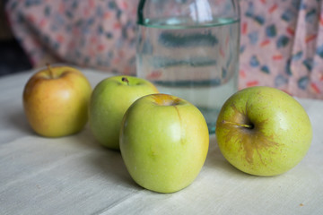 Still life with green apples and .water bottle on the table. Apples lie on a background of drapery