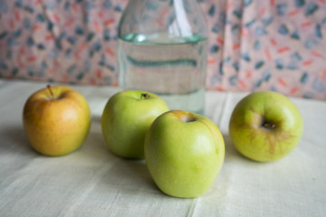 Still life with green apples and .water bottle on the table. Apples lie on a background of drapery