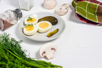 Half boiled eggs, sprinkled with pepper and dill and chopped pickles on a white wooden board