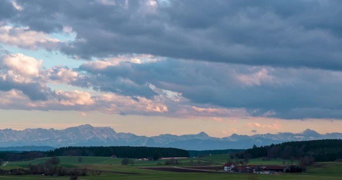 Time lapse of moving clouds on late evening above a rural landscape wit the alps in the background.
