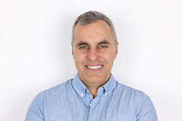 portrait of adult handsome man with grey hair wearing blue shirt standing on isolated white background