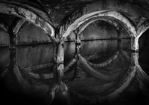 Antiguo deposito de agua abandonado con reflejo del techo y columnas en el agua.