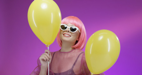 Girl with pink hair having fun with yellow ballons.