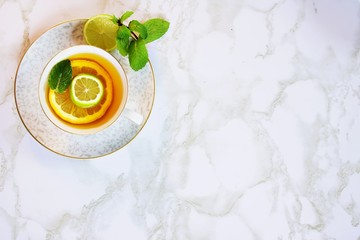Marble background with tea cup.  Lemon and lime slices in the tea cup with a mint leaf.  A lime slice with mint leaves are placed on the saucer.  
