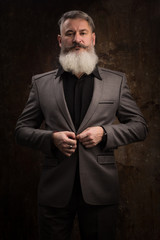 Portrait of a Middle Age Man with Beard and Mustache Posing in Formal Wear on a Dark Backdrop, selective focus