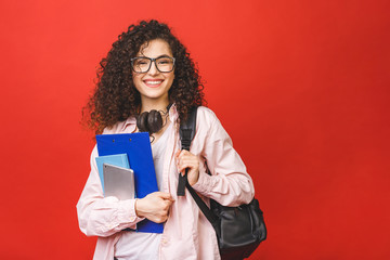 Young curly student woman wearing backpack glasses holding books and tablet over isolated red...