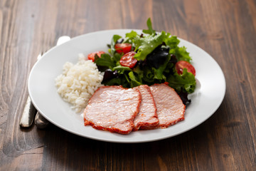 fried pork with boiled rice and salad on white plate on brown wooden background