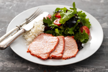 fried pork with boiled rice and salad on white plate on ceramic background