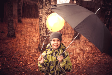 A teenage boy walks with an umbrella and a Golden yellow balloon in the rain. The balloon is like the sun. The boy laughs, rejoices, is happy. A child hides a balloon under an umbrella.