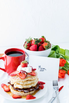 A vertical view of a tray table filled with breakfast items, a card and flowers for Mother's Day.
