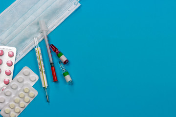 medical protective mask with medicines, syringe and thermometer on a blue background, copy spaсe
